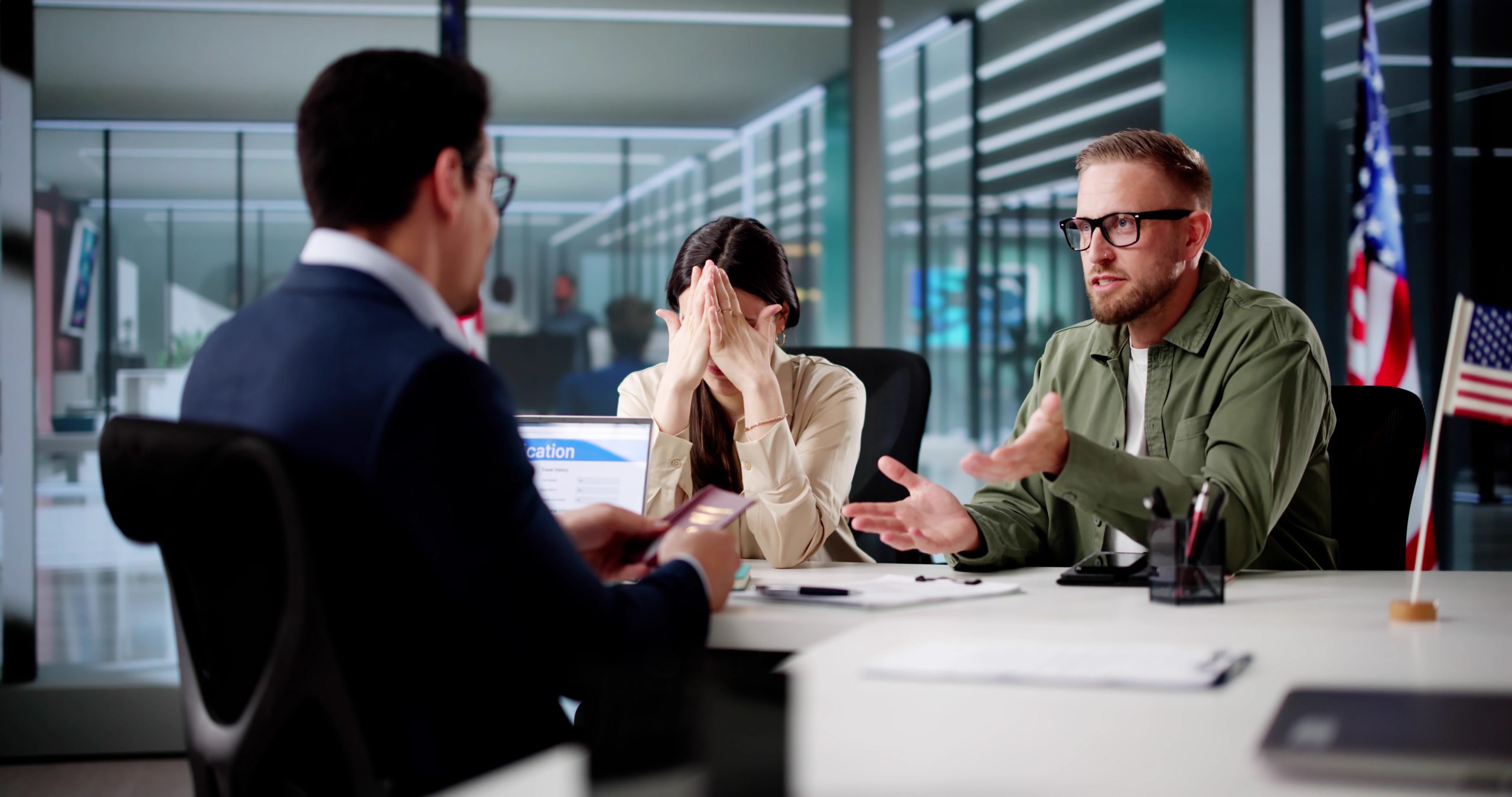 A man and woman consult a lawyer in a modern office with small U.S. flags on the desk.